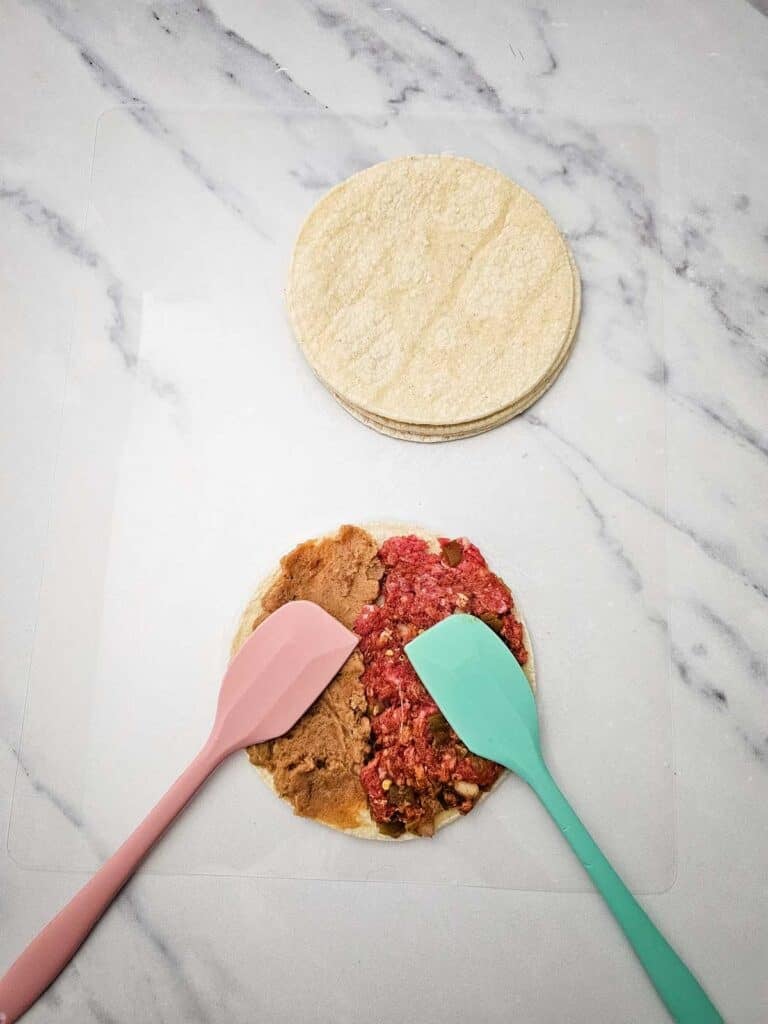 spreading meat and refried beans on a tortilla