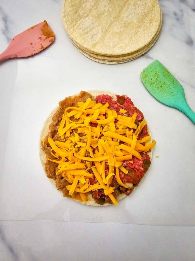 shredded cheese on top of meat mixture on a tortilla