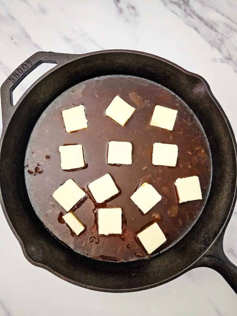 pats of butter on top of french onion soup, beef consomme and rice in a skillet