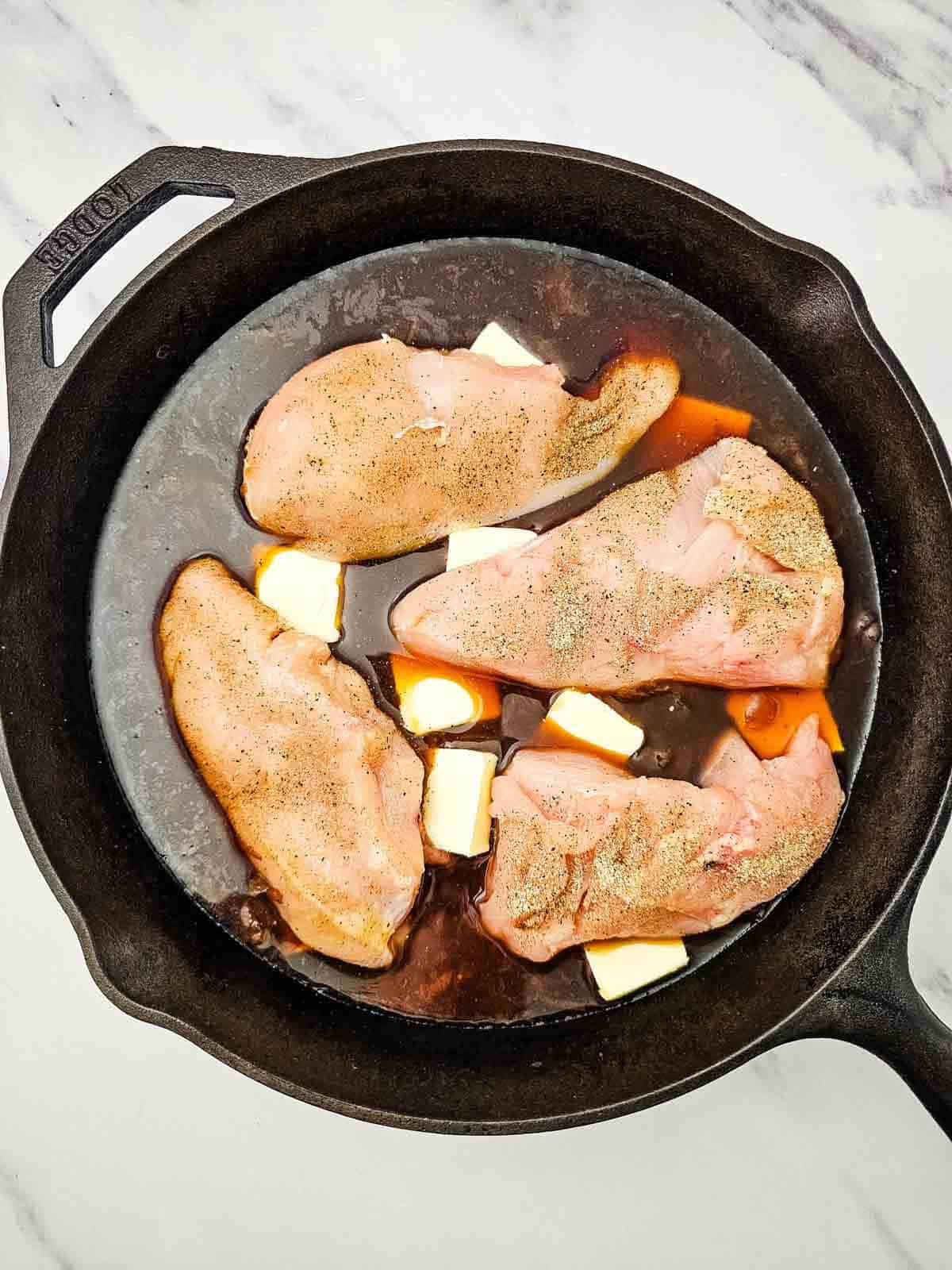 seasoned chicken breasts on top of butter and french onion soup in a skillet