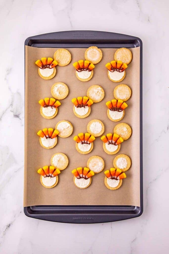 attaching candy corn to the filling of golden oreos on a baking sheet