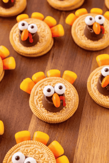These Golden Oreo Turkey Cookies are the cutest no bake Thanksgiving treat for kids and adults. Made with Golden Oreos, Rolos, candy corn, candy eyeballs, Reese's Pieces and red decorating icing, these easy turkey cookies are perfect for Thanksgiving dessert tables, classroom parties, holiday baking trays and fun fall food ideas. This simple Oreo turkey cookie recipe comes together in about 20 minutes with melted chocolate candy melts holding everything in place. If you need Thanksgiving cookies, cute turkey desserts, no bake fall treats, Golden Oreo desserts, Thanksgiving party food, edible turkey crafts or easy holiday recipes kids can help decorate, these adorable Golden Oreo and Rolo turkeys are a festive little win for your holiday spread.