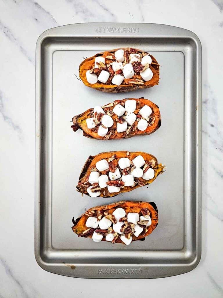marshmallows on top of baked sweet potatoes on a baking sheet