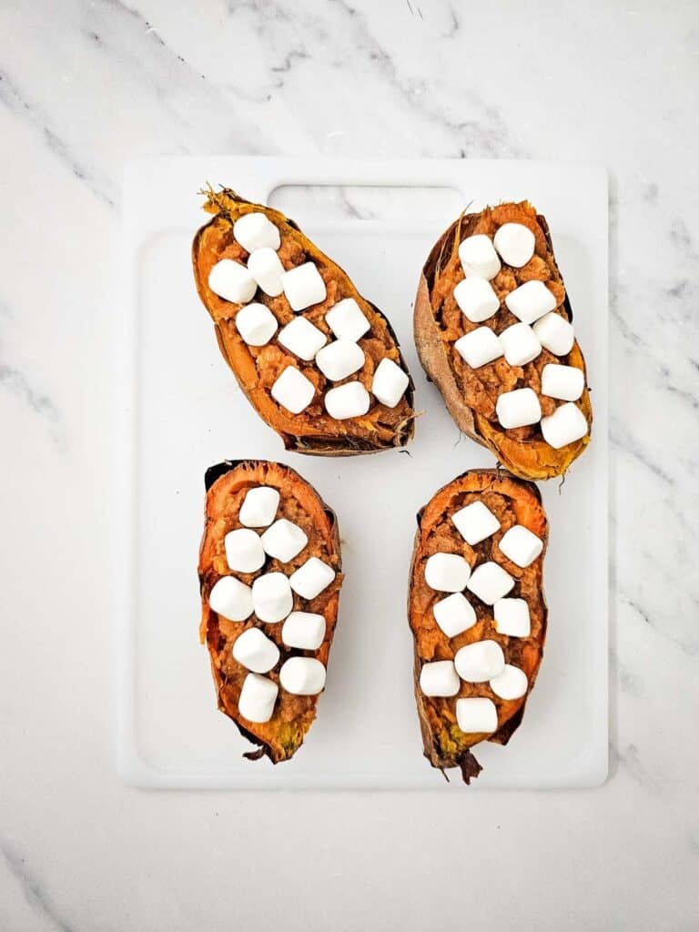 marshmallows on top of baked sweet potatoes on a cutting board