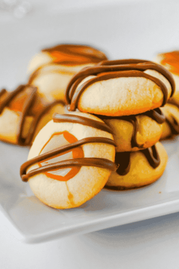 These Twix Cookies are buttery shortbread-style cookies filled with gooey caramel and drizzled with melted milk chocolate for an easy candy bar inspired dessert. This Twix Cookies recipe is perfect for Christmas cookies, holiday cookie trays, bake sales, parties, potlucks and sweet treats for caramel lovers. Made with simple ingredients like butter, sugar, egg yolks, vanilla, caramel bits, heavy cream and chocolate chips, these caramel chocolate cookies are fun to make and even better to eat. If you love easy cookie recipes, thumbprint cookies, shortbread cookies, chocolate caramel cookies or homemade Twix desserts, these sweet little cookies are a must bake for your next dessert table or cookie exchange.