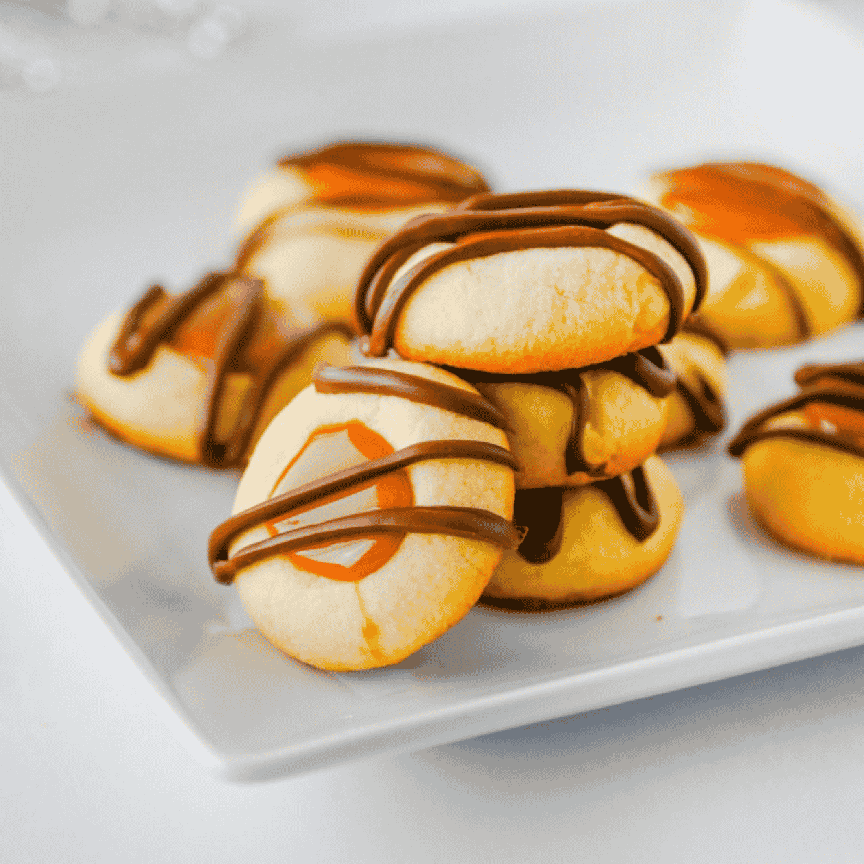 These Twix Cookies are buttery shortbread-style cookies filled with gooey caramel and drizzled with melted milk chocolate for an easy candy bar inspired dessert. This Twix Cookies recipe is perfect for Christmas cookies, holiday cookie trays, bake sales, parties, potlucks and sweet treats for caramel lovers. Made with simple ingredients like butter, sugar, egg yolks, vanilla, caramel bits, heavy cream and chocolate chips, these caramel chocolate cookies are fun to make and even better to eat. If you love easy cookie recipes, thumbprint cookies, shortbread cookies, chocolate caramel cookies or homemade Twix desserts, these sweet little cookies are a must bake for your next dessert table or cookie exchange.