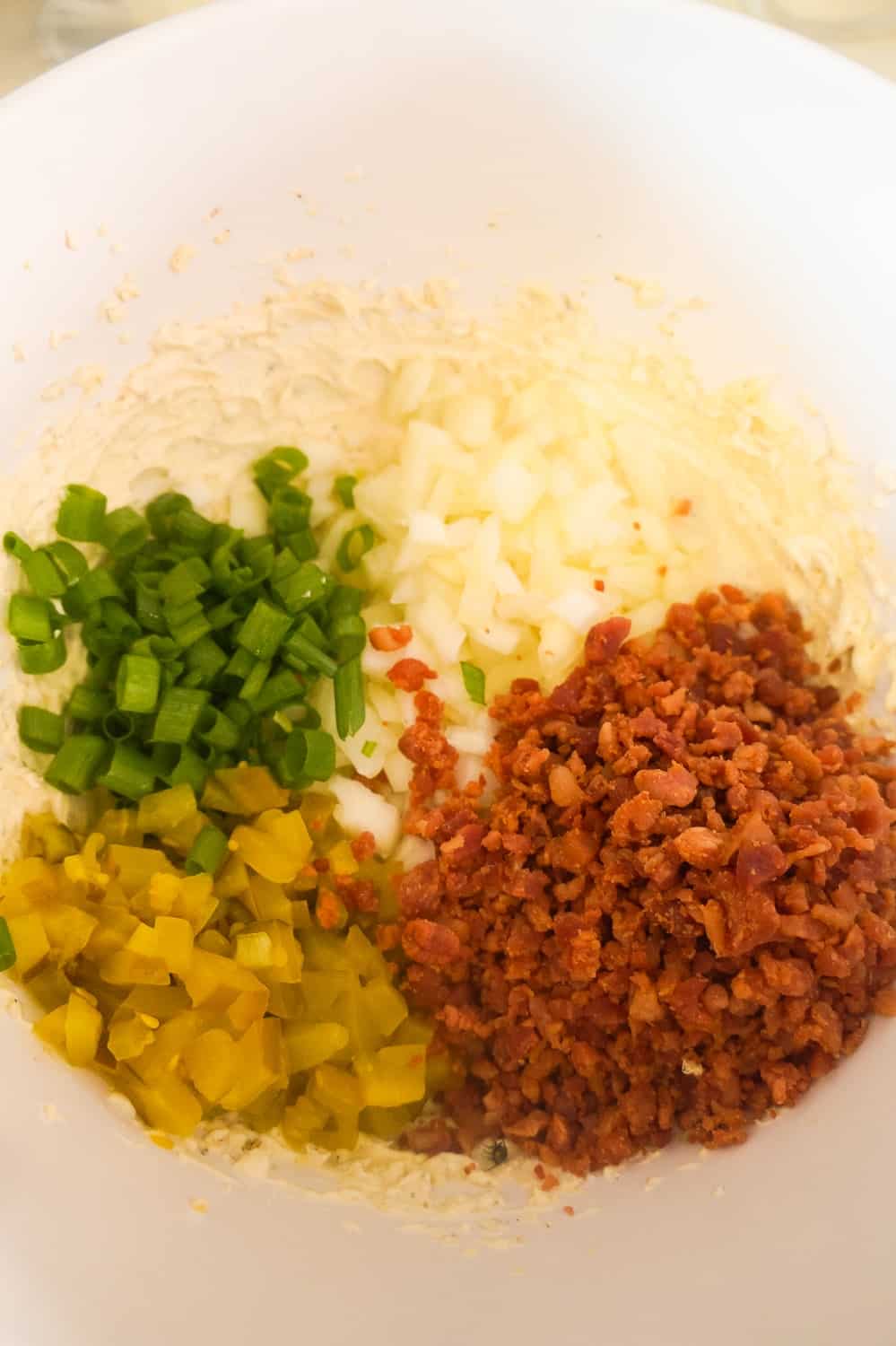 diced onion, chopped green onion, diced pickles and real bacon bits in a mixing bowl with herb and garlic cream cheese.