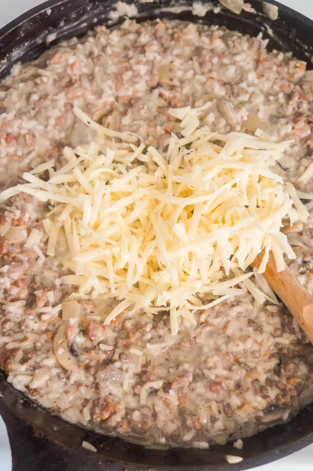 pile of shredded Swiss cheese on top of ground beef and rice