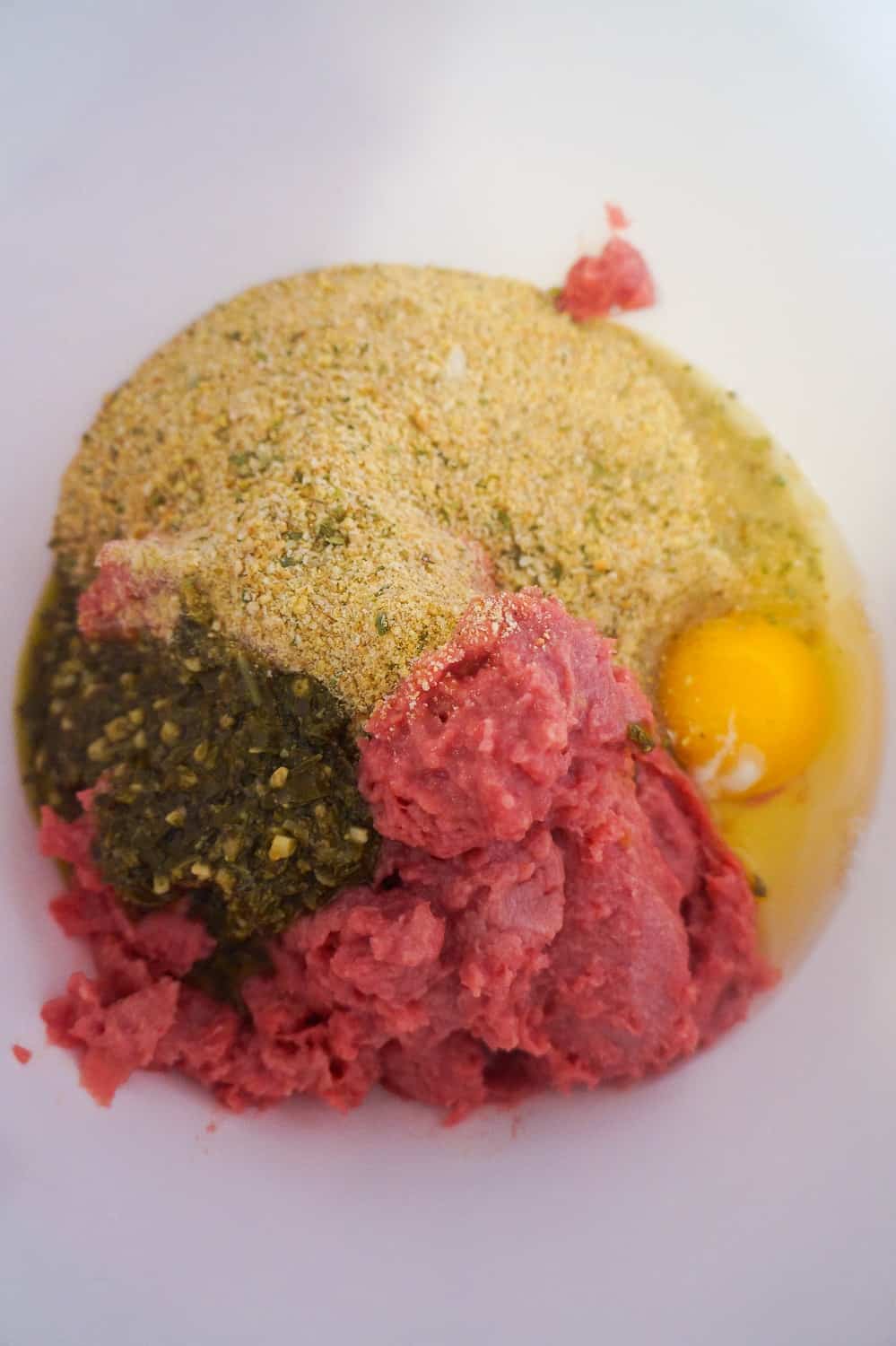 ground chicken in a bowl with bread crumbs, egg and basil pesto