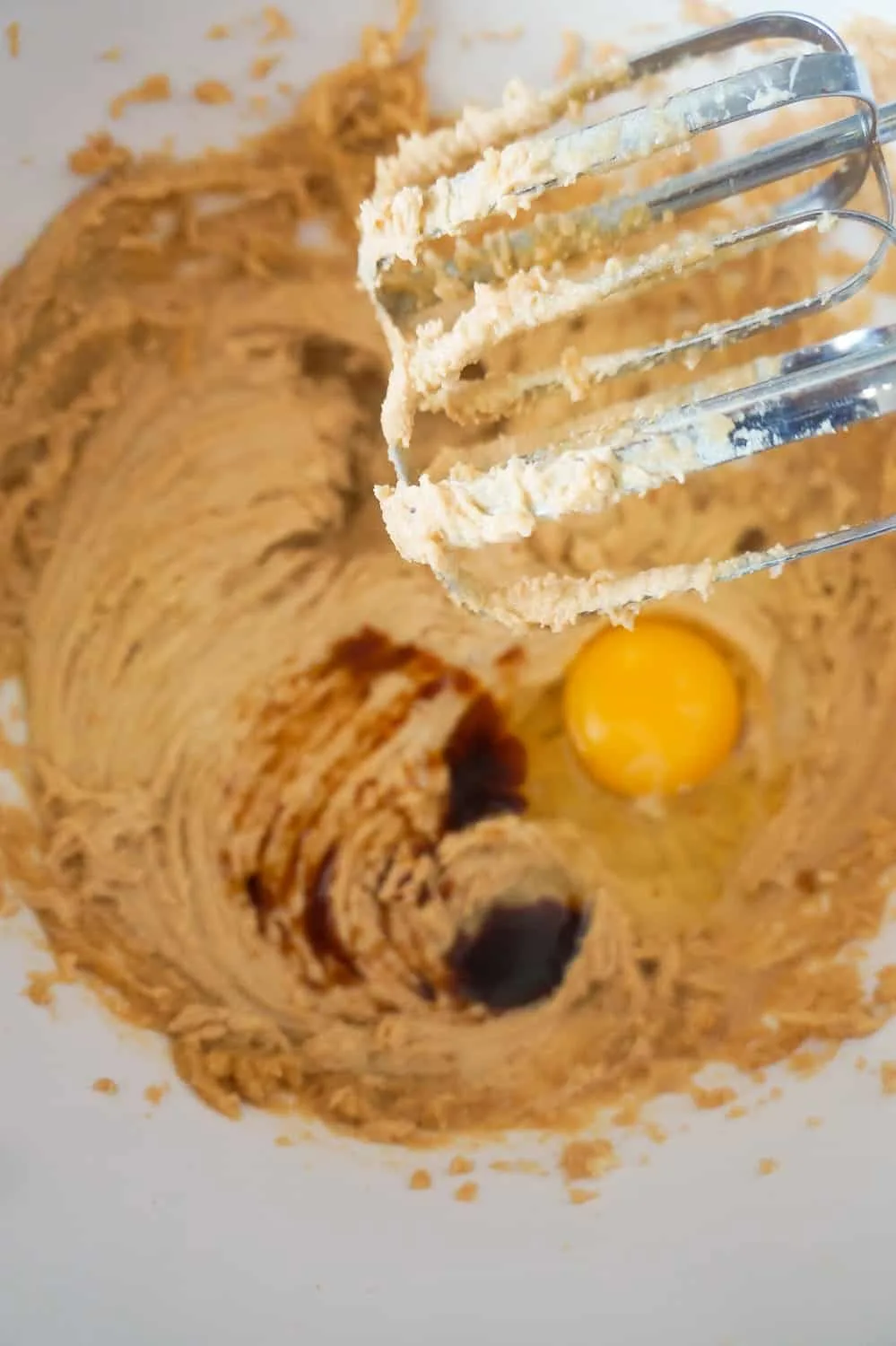 eggs and vanilla being added to peanut butter cookie dough in mixing bowl