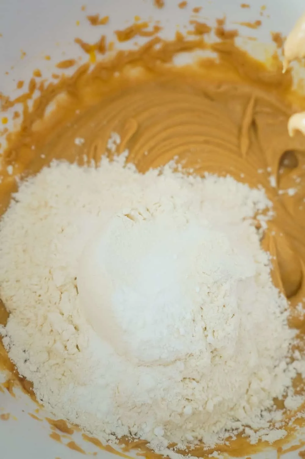 flour and baking powder added to peanut butter cookie dough in mixing bowl