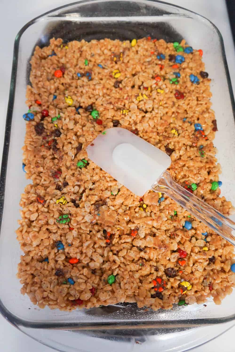 peanut butter rice krispies being pressed into baking dish