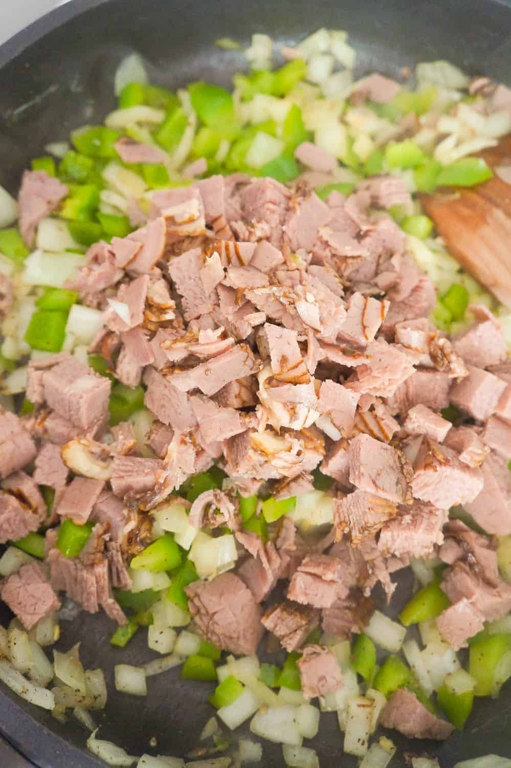 chopped roast beef added to diced green peppers and diced onions in a frying pan