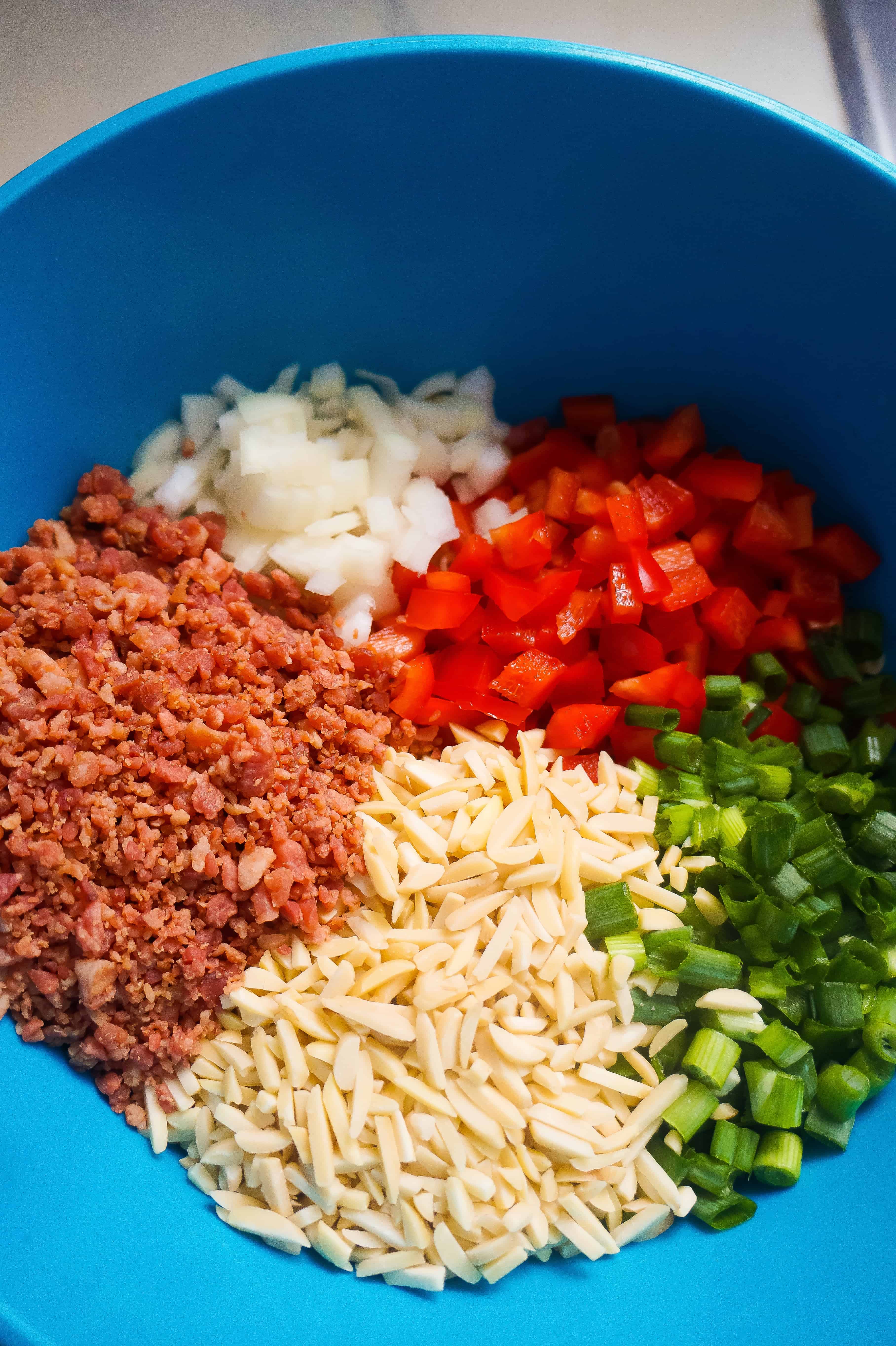 Bowl with macaroni, red peppers, bacon bits, almonds and onions