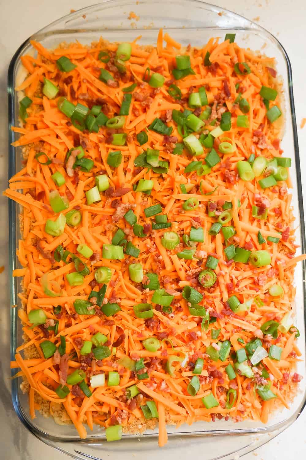 shredded cheddar cheese, chopped green onions and bacon bits on top of a mashed potato casserole