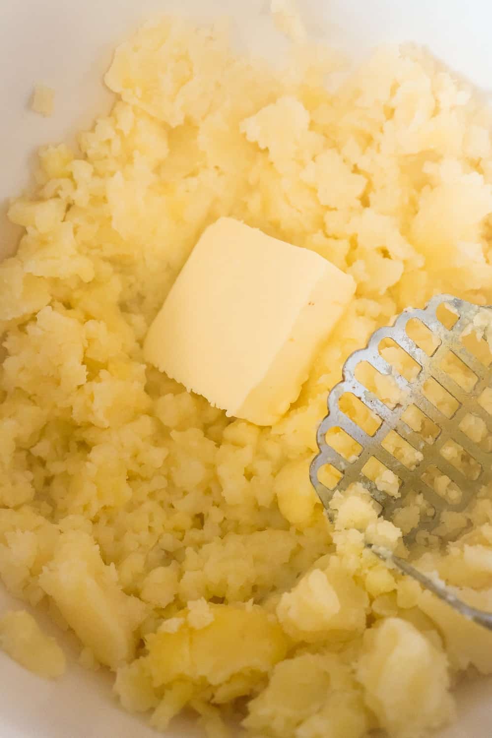 butter and milk added to mashed potatoes in a mixing bowl