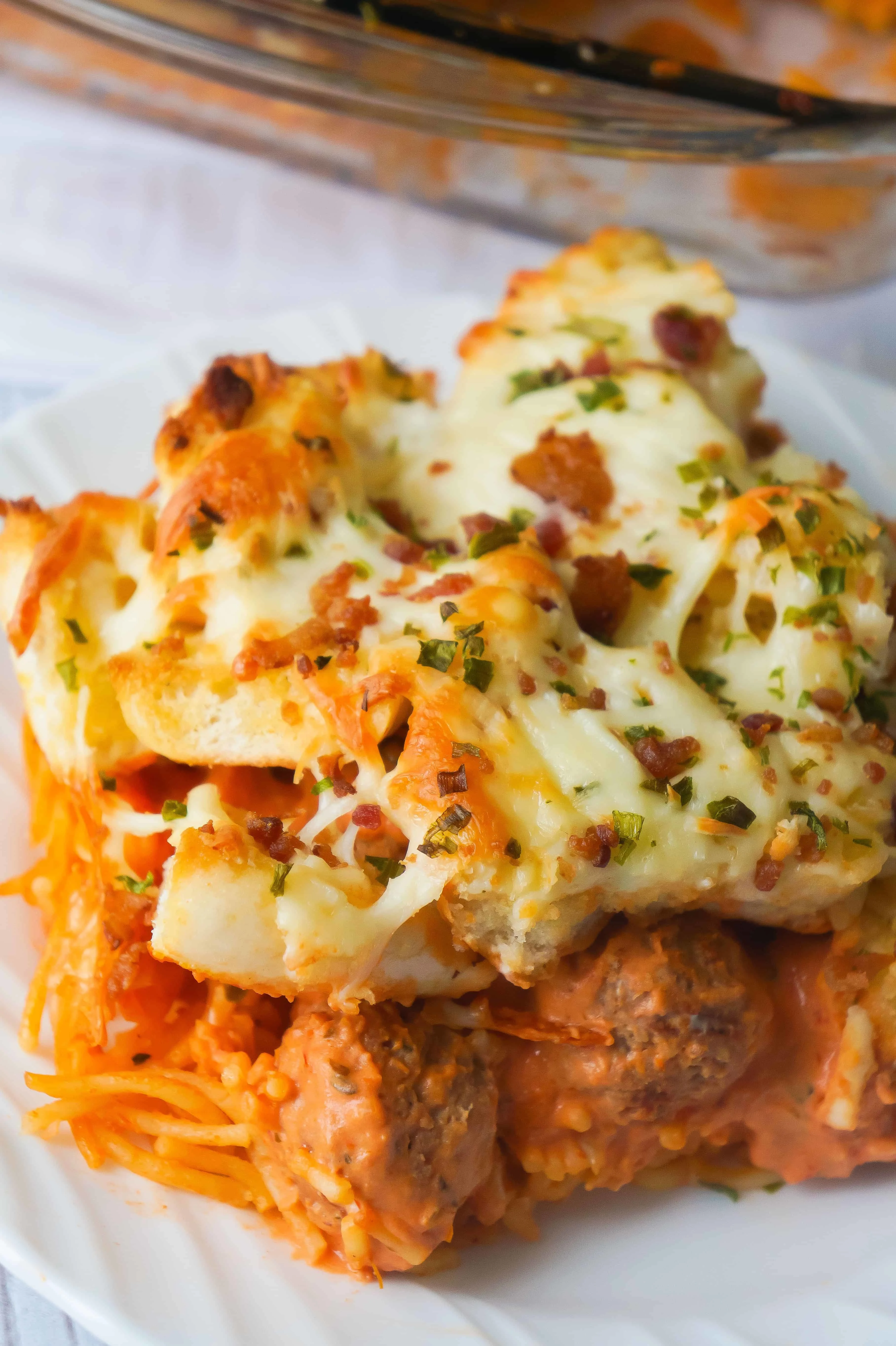 This baked spaghetti and meatballs casserole is topped with garlic cheese bread. This easy dinner recipe is made with meatballs and spaghetti in a cream cheese and marinara sauce followed by a layer of bagel pieces coated with garlic butter and topped with cheese and bacon bits.